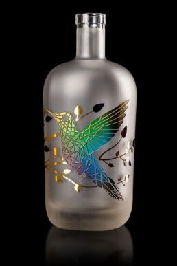 Gravure d'un colibri sur une bouteille satinée et décorée d'un marquage à chaud, multi couleurs fondues.
